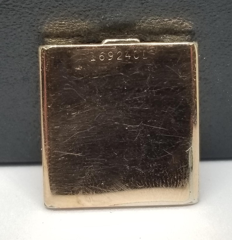Puede incluir: Un objeto rectangular de metal dorado con el n&uacute;mero "169240L" grabado en la superficie. El objeto tiene un aspecto ligeramente desgastado, con ara&ntilde;azos e imperfecciones visibles. Probablemente sea un componente de una pieza m&aacute;s grande, como un reloj o una joya.