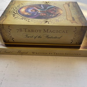 May include: A gold box with the text "78 Tarot Magical Tarot of the Fantastical" on the front. The box is sitting on top of a book with the text "78 Tarot Magical - Written by Trish Sullivan" on the front.