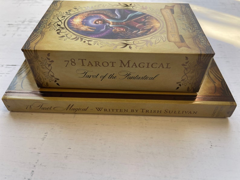 May include: A gold box with the text "78 Tarot Magical Tarot of the Fantastical" on the front. The box is sitting on top of a book with the text "78 Tarot Magical - Written by Trish Sullivan" on the front.
