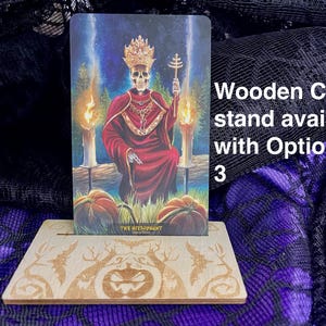 K&ouml;nnte beinhalten: Ein Kartenst&auml;nder aus Holz mit einem geschnitzten K&uuml;rbisdesign. Der St&auml;nder zeigt eine Tarotkarte mit einer skelettartigen Figur in einem roten Gewand und einer Krone. Die Karte lautet "Der Hierophant".
