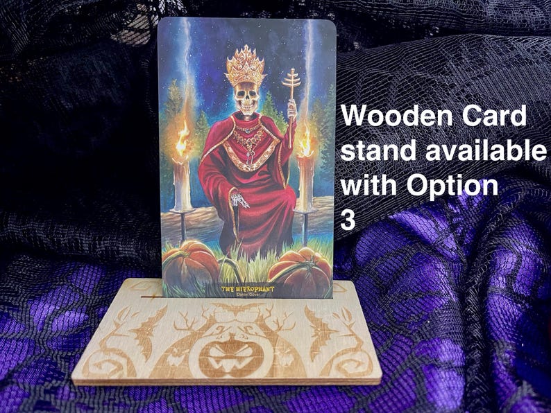 K&ouml;nnte beinhalten: Ein Kartenst&auml;nder aus Holz mit einem geschnitzten K&uuml;rbisdesign. Der St&auml;nder zeigt eine Tarotkarte mit einer skelettartigen Figur in einem roten Gewand und einer Krone. Die Karte lautet "Der Hierophant".