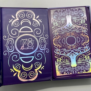 May include: A purple box with a holographic design featuring the text "78 Tarot Animal". The box is open to reveal a card with a holographic design of a tree with intricate details.