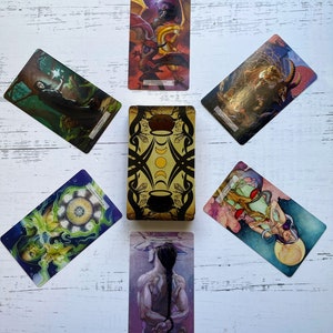 May include: Tarot card spread with ten cards laid out in a cross pattern on a white wooden surface. The cards feature colorful illustrations of mythical creatures, celestial bodies, and other symbolic imagery.