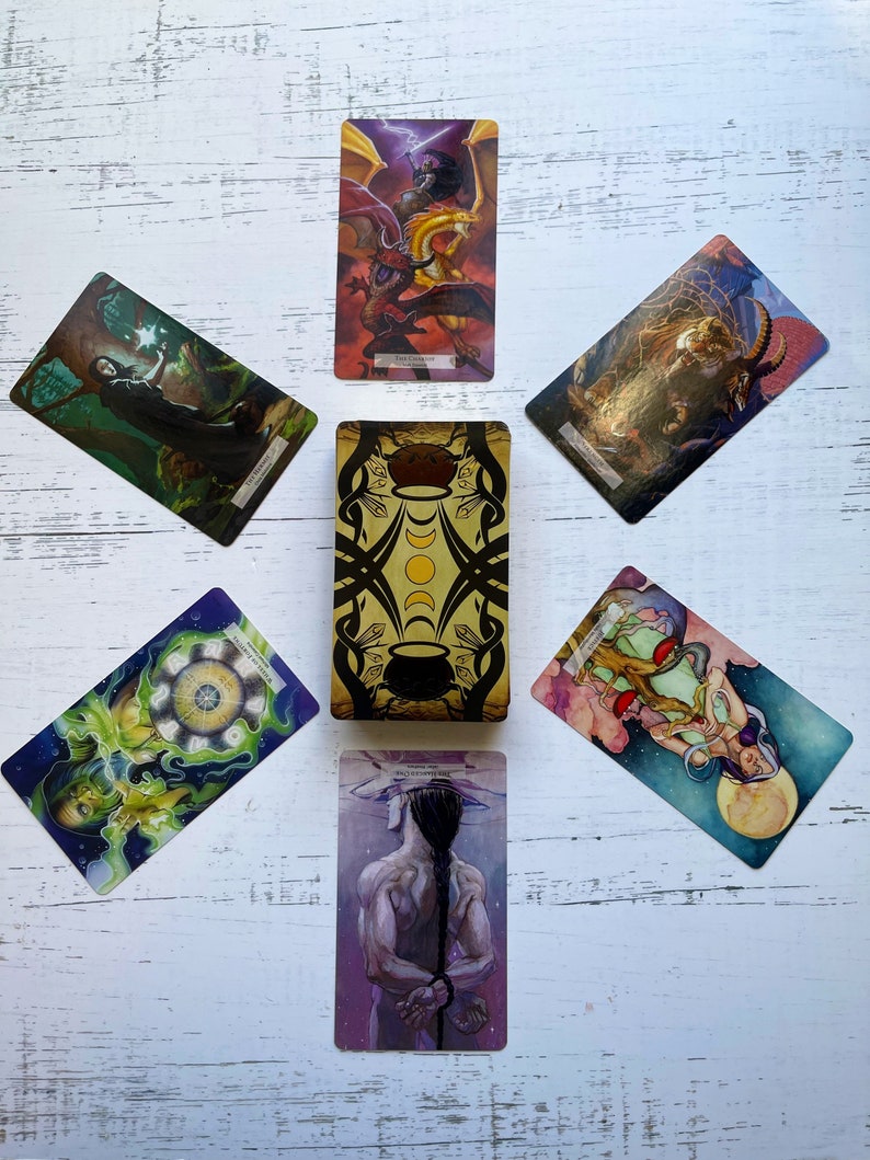 May include: Tarot card spread with ten cards laid out in a cross pattern on a white wooden surface. The cards feature colorful illustrations of mythical creatures, celestial bodies, and other symbolic imagery.