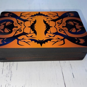 K&ouml;nnte beinhalten: Ein Kartenspiel mit Halloween-Motiv. Die Karten haben ein schwarzes und orangefarbenes Design mit Flederm&auml;usen und K&uuml;rbissen.