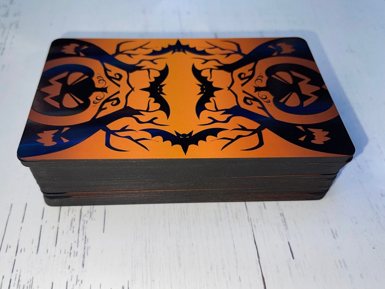 K&ouml;nnte beinhalten: Ein Kartenspiel mit Halloween-Motiv. Die Karten haben ein schwarzes und orangefarbenes Design mit Flederm&auml;usen und K&uuml;rbissen.