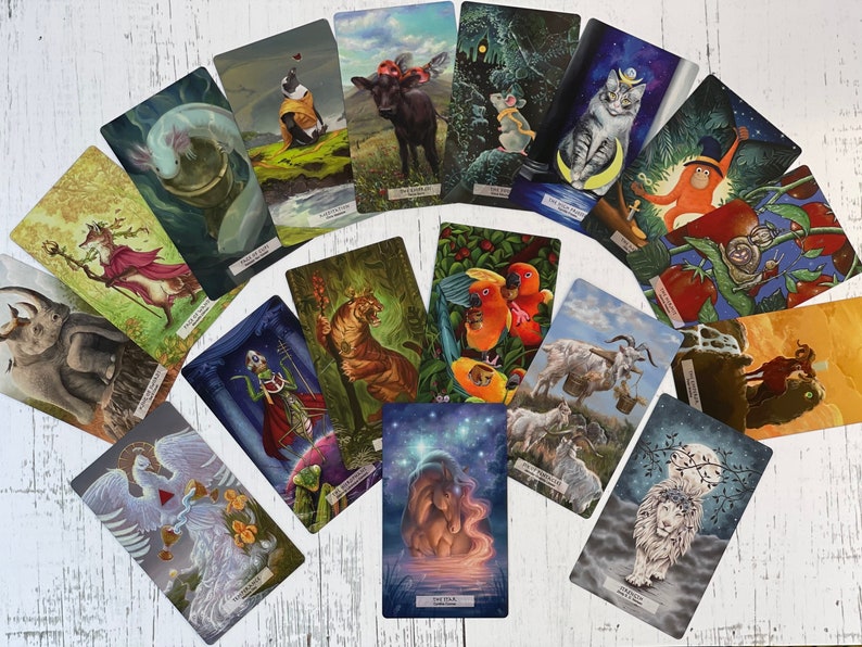 May include: A set of 15 tarot cards featuring colorful illustrations of animals and mythical creatures. The cards are arranged in a circle on a white wooden surface. The cards are part of a larger deck of tarot cards.