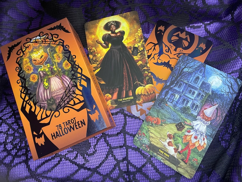 K&ouml;nnte beinhalten: Ein Set mit 78 Tarotkarten mit Halloween-Thema. Die Schachtel ist orange mit schwarzen Flederm&auml;usen und einem Spinnennetz-Design. Die Karten zeigen Illustrationen einer Hexe, eines Spukhauses und eines K&uuml;rbisses.