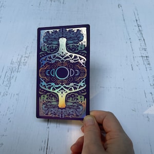 May include: A purple card with a holographic design featuring a tree with branches and leaves. The tree is surrounded by a circle with the word "GOD" written in it. The card has a rainbow iridescent finish.