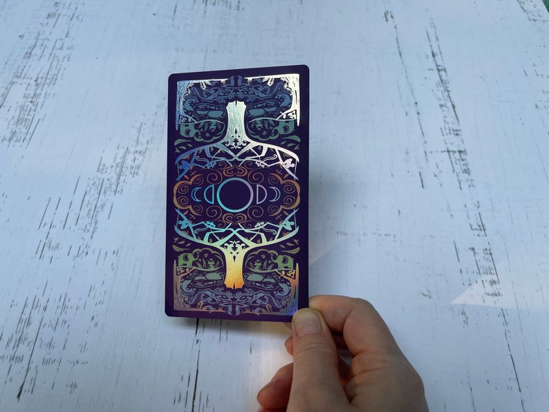 May include: A purple card with a holographic design featuring a tree with branches and leaves. The tree is surrounded by a circle with the word "GOD" written in it. The card has a rainbow iridescent finish.