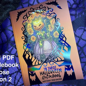 K&ouml;nnte beinhalten: Ein kupferfarbenes Handbuch mit einem holografischen Cover, das eine schwarze Silhouette einer Sonnenblume mit einem Gesicht zeigt. Der Text auf dem Cover lautet "78 Tarot Halloween Guidebook" und "Written by Trish Sullivan".