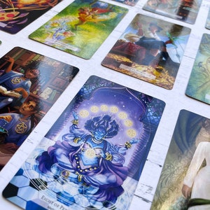 May include: A tarot card deck with colorful illustrations of people, animals, and symbols. The cards are laid out on a white surface. The card in the center shows a blue figure with a crown and a purple robe, surrounded by eight golden coins. The card text reads "Eight of Pentacles".