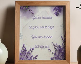 Op de afbeelding: Een rechthoekige houten lijst met een witte print en paarse lavendeltakjes in de hoeken. De tekst in het midden luidt: You've survived all your worst days. You can survive this one too. De lijst heeft een lichtbruine afwerking.