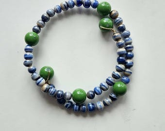 May include: A multi-strand wrap bracelet featuring a series of small, round, blue and white striped beads interspersed with larger, smooth, solid green beads. The beads are strung on a flexible wire, creating a circular, layered coil design.