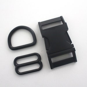 May include: A collection of black hardware components, comprising a D-ring, a tri-glide slide, and a side-release buckle. These are commonly used in crafting and sewing, suitable for bags, straps, and other accessories.