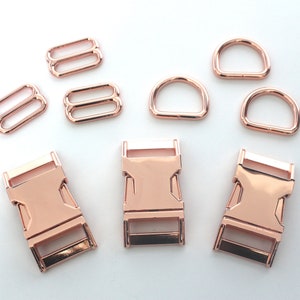 May include: Rose gold metal hardware set including D-rings, slide adjusters, and side-release buckles. The set is ideal for crafting dog collars, bag straps, or other DIY projects. The hardware has a shiny, metallic finish.