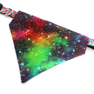 May include: A dog bandana with a vibrant galaxy print in shades of red, green, blue, and yellow. The bandana is attached to a black collar with a colorful geometric pattern and a black plastic buckle.