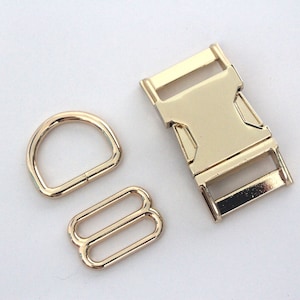 May include: A collection of three gold-coloured metal hardware components. The set includes a D-ring, a slide adjuster, and a side-release buckle. These findings are suitable for bag making, pet collars, or other craft applications.
