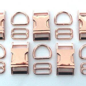 May include: Rose gold metal hardware set including buckles, D-rings, and tri-glide slides. The set is arranged on a white surface. The hardware is likely for use in crafting or pet accessories.
