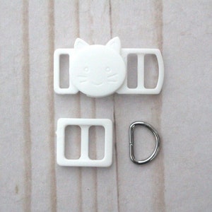 May include: White plastic cat-shaped slider buckle with two white plastic strap adjusters and a silver metal D-ring.