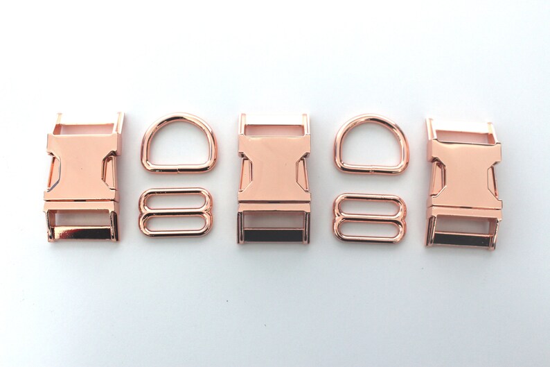 May include: Rose gold metal hardware set including buckles, D-rings, and rectangular rings. The set is displayed on a white background. These components are commonly used in crafting and accessories.
