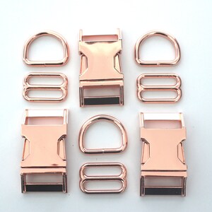 May include: Rose gold metal hardware set, including D-rings, slide adjusters, and side-release buckles. The hardware is arranged on a white surface, showcasing the shiny, metallic finish. Ideal for crafting pet collars, bags, or other accessories.