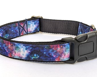 May include: A black dog collar with a vibrant galaxy print in shades of blue, purple, and pink. The collar features a black plastic buckle and metal hardware for adjusting the size. The collar is designed for pets.