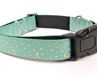 Puede incluir: Un collar para perros turquesa con un patrón repetido de estrellas y lunas crecientes doradas. El collar tiene una hebilla de plástico negro y un respaldo de nailon negro. El collar mide aproximadamente 2,5 cm de ancho.