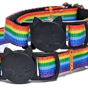 May include: Two cat collars featuring rainbow stripes and black cat-shaped buckles. The collars have a black nylon backing and silver-coloured metal hardware for attaching a lead. The rainbow stripes include red, orange, yellow, green, blue, and purple.