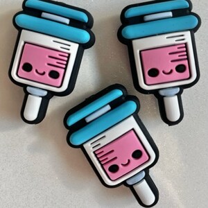 May include: Three blue and white syringe charms with pink liquid and a smiling face. The charms are made of silicone and are perfect for adding a fun and quirky touch to your accessories.