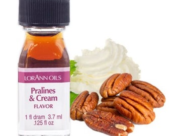 May include: A small glass bottle with a brown liquid inside. The bottle has a black cap and a white label that says "Lorann Oils Pralines & Cream Flavor 1 fl dram 3.7 ml .125 fl oz". The bottle is sitting on a white surface with whipped cream and pecans.