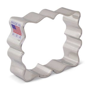 May include: A silver metal cookie cutter shaped like a wavy rectangle. The cutter has a label that says "Made in U.S.A." with a small American flag.