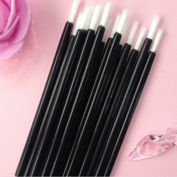 May include: A bunch of black disposable mascara wands with white tips. The wands are arranged in a stack, with the tips facing up.