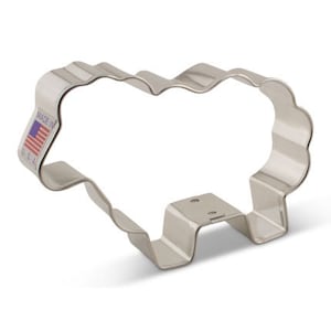 May include: A silver metal cookie cutter shaped like a sheep. The cutter has a wavy edge and a small handle on the bottom. The cutter is made in the USA.