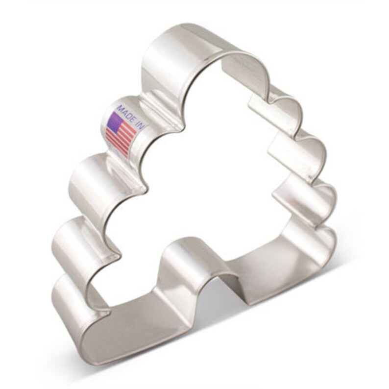 May include: A shiny, silver-colored cookie cutter in the shape of a Christmas tree. The cutter has a wavy design and a small tag that reads "MADE IN" with a small American flag.