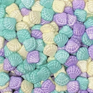 May include: A collection of pastel-colored seashell sprinkles. The sprinkles are in shades of light blue, lavender, and white.