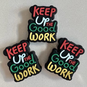 May include: Three black and yellow shoe charms with the text "Keep Up The Good Work" in red, white, green, and yellow lettering.