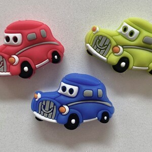May include: Three toy cars in red, blue, and green. Each car has a smiling face and a simple design.
