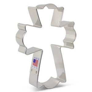 May include: A silver metal cookie cutter shaped like a cross with a scalloped edge. The cutter is made in the USA.