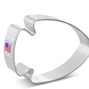 May include: A silver metal cookie cutter shaped like an American football. The cutter has a smooth, rounded surface and is made in the USA.