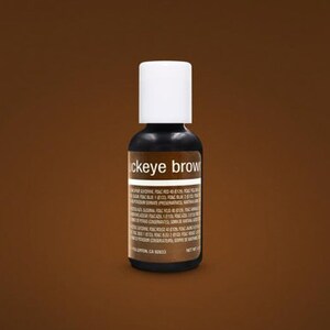 May include: A small, dark brown bottle with a white cap, labeled "Buckeye Brown." The bottle contains a liquid and has a label with ingredient information. The background is a solid, medium brown.