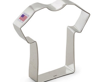 May include: A silver metal cookie cutter shaped like a t-shirt. The cookie cutter has a label that says "Made in USA".
