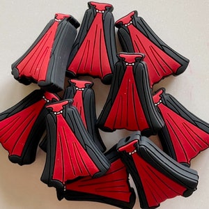 May include: A group of ten red and black Halloween costume charms in the shape of a cape. The capes have a black collar and a red body with a white pearl necklace.