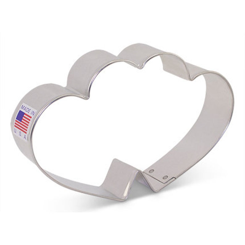 May include: A silver metal cookie cutter shaped like a cloud with two rounded peaks. The cutter has a "Made in USA" label on the side.