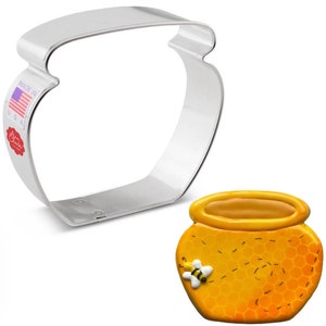 May include: A silver metal cookie cutter shaped like a honey pot with a small bee and honeycomb design on the side.  The cookie cutter is next to a decorated cookie in the shape of a honey pot.