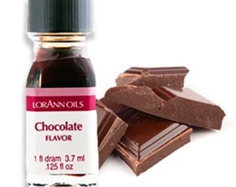 May include: A small glass bottle with a black cap containing chocolate flavoring. The bottle is labeled "Lorann Oils Chocolate Flavor" and contains 1 fl dram (3.7 ml) or .125 fl oz. The bottle is sitting on a white surface with a pile of broken chocolate bars in the background.