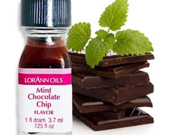 May include: A small glass bottle of Lorann Oils Mint Chocolate Chip flavoring. The bottle is filled with a dark brown liquid and has a white cap. The label is pink and white and says "Lorann Oils Mint Chocolate Chip Flavor 1 fl dram 3.7 ml 1/25 fl oz". The bottle is sitting on a stack of dark chocolate squares with a sprig of green mint leaves on top.