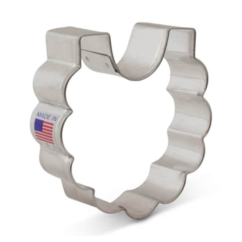 May include: A silver metal cookie cutter shaped like a baby bib with a scalloped edge. The cutter has a "Made in USA" label on the side.