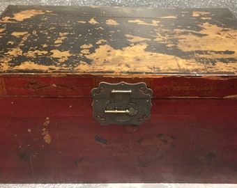 May include: A rectangular antique chest with a red body and a distressed black top. The chest features a metal lock and decorative corner accents. The wood shows signs of age and wear, adding to its vintage appeal.