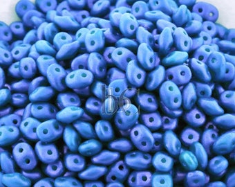 May include: A bowl filled with small, blue, teardrop-shaped beads. The beads have a matte finish and are arranged in a random pattern.
